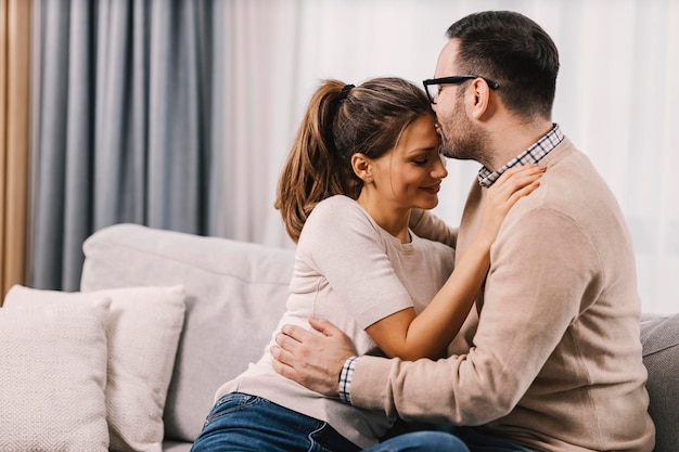 Couple dans un salon, l'homme embrasse le front de sa femme