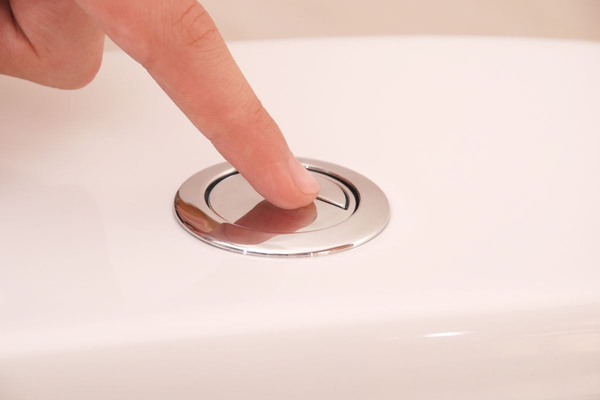 Gros plan sur une main appuyant sur le bouton d'une chasse d'eau