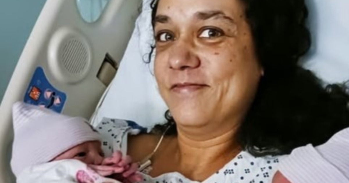 Femme d'âge mûr tenant des vêtements de bébé, l'air à la fois surprise et pensive